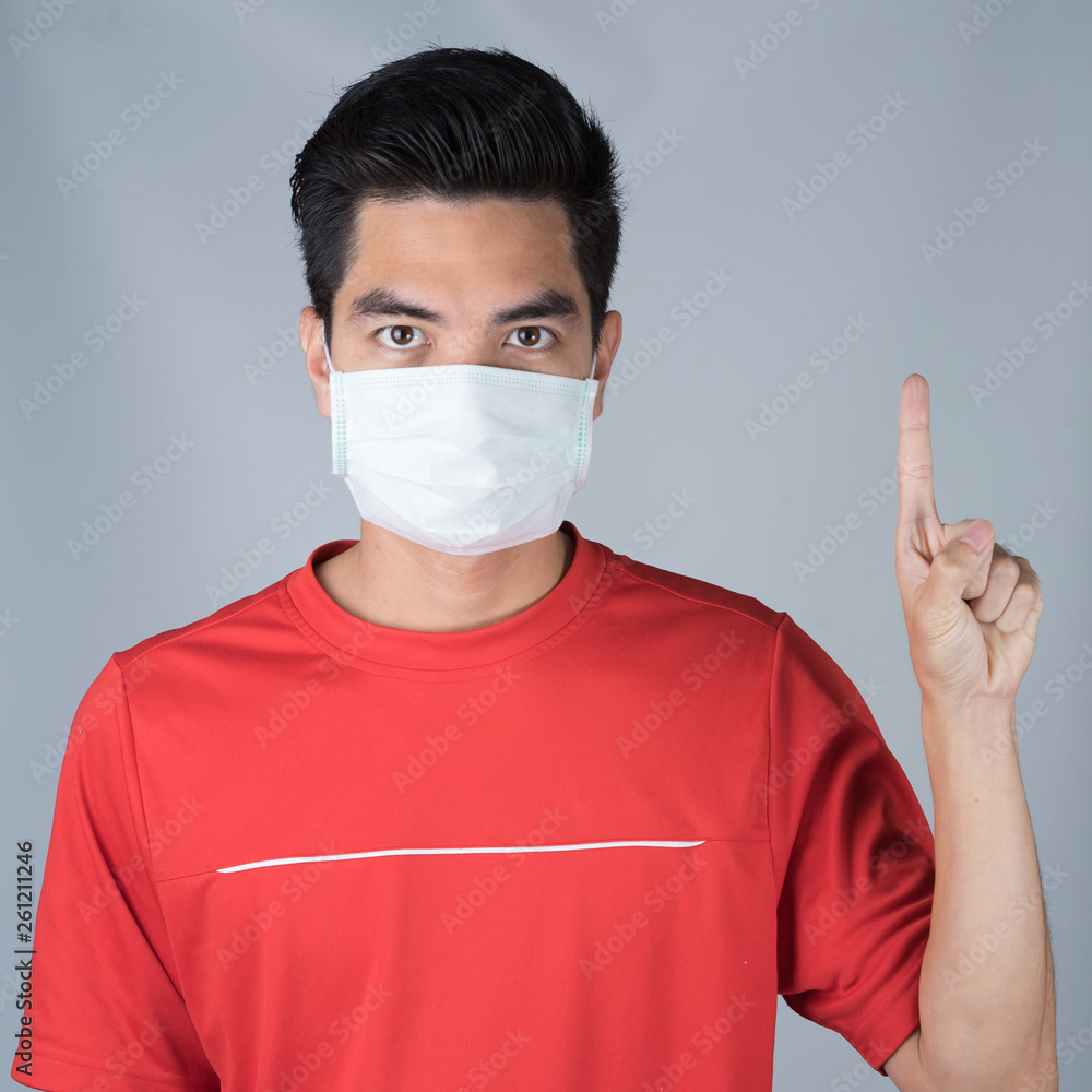 Sick young man wearing medical mask and red shirt thumbs up sign isolated on gray wall background. Concept of headache. Asia people. Sick young man wearing medical mask and red shirt thumbs up sign isolated on gray wall background. Concept of headache. Asia people.