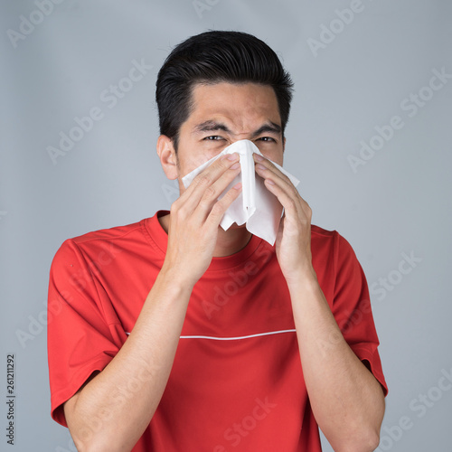Sick young man handsome and sneeze wearing medical mask and red shirt isolated on gray wall background. Concept of sick. Asia people.