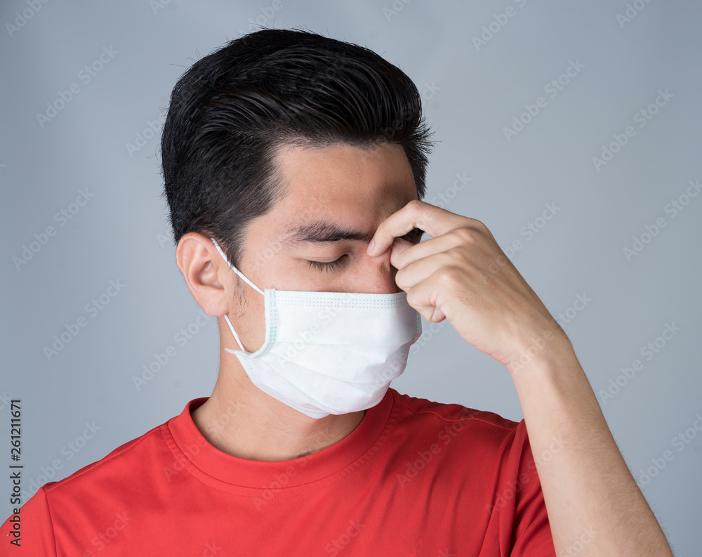 Sick young man handsome and headache wearing medical mask and red shirt isolated on gray wall background. Concept of headache. Asia people. Sick young man handsome and headache wearing medical mask and red shirt isolated on gray wall background. Concept of headache. Asia people.