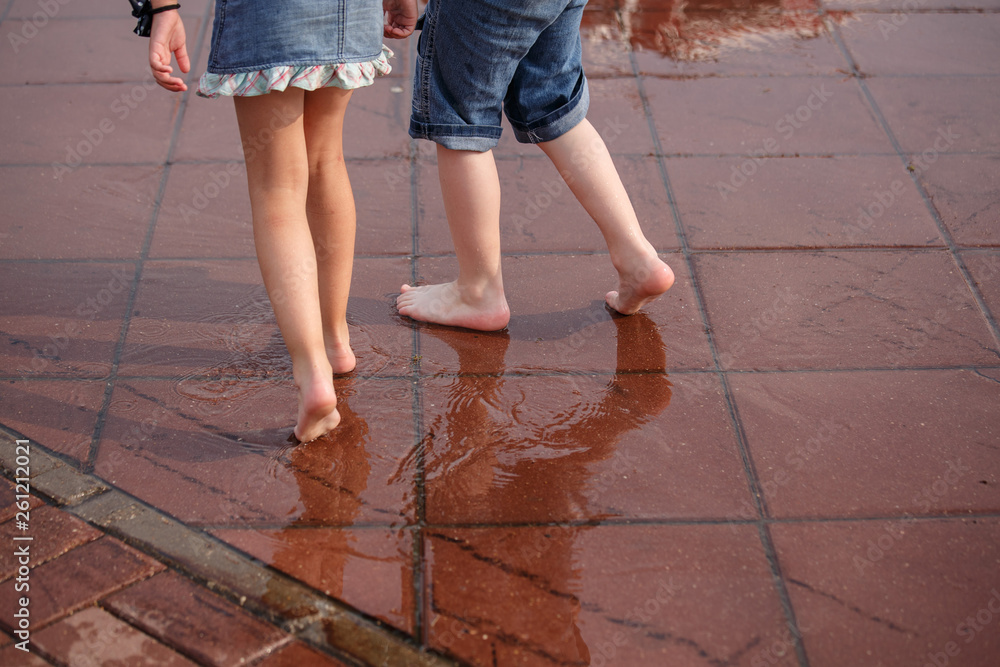 Children, boy and girl, running barefoot through puddles. The concept of happy childhood, summer vacation, friendship.