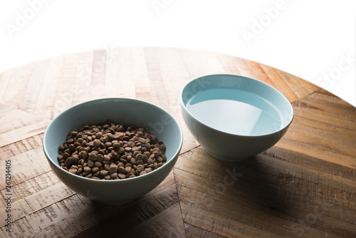 cat food dishes - two blue bowls of cat dry food and water standing on a wooden table in front of white background