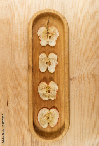 Four dried apple slices on oblong wooden plate on natural wooden background.