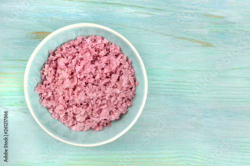 A bowl of pink Himalayan sea salt, shot from above on a teal blue background with copy space