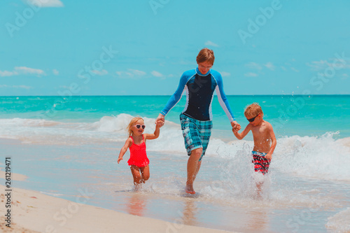 happy father with little son and daughter play with water at beach