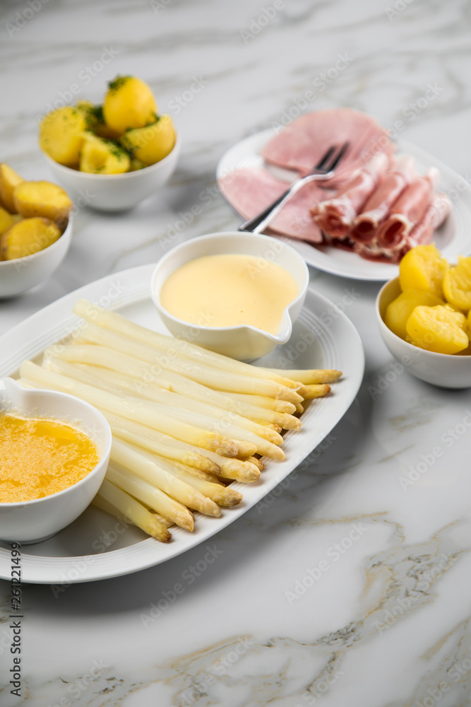 Platte weißer Spargel mit Sauce Hollandaise, zerlassener Butter, Kochschinken, geräucherten Schinken und Kartoffeln auf Marmor Hintergrund Platte weißer Spargel mit Sauce Hollandaise, zerlassener Butter, Kochschinken, geräucherten Schinken und Kartoffeln auf Marmor Hintergrund