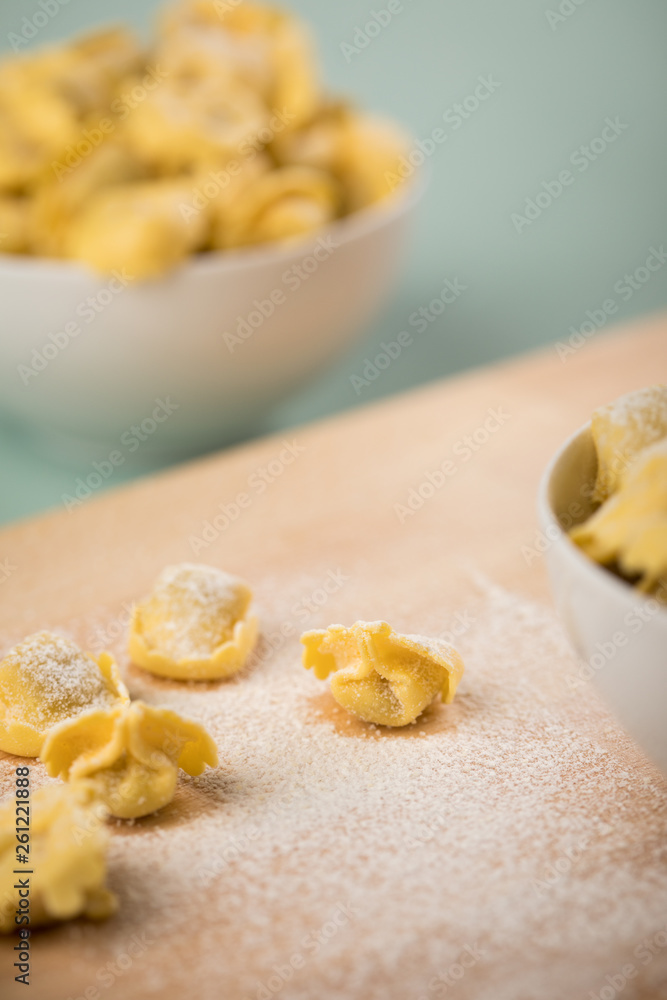 Frische, rohe Cappelletti Tortellini Pasta mit Mehl und Grieß in Porzellan Schale auf Holz Brett und Pastell Grün Hintergrund Frische, rohe Cappelletti Tortellini Pasta mit Mehl und Grieß in Porzellan Schale auf Holz Brett und Pastell Grün Hintergrund