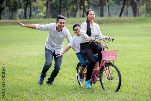 happy asian Family, parents and their children riding bike in park together. father pushes mother and son on bicycle having fun and laughing outside Support helps . cheerful . leisure