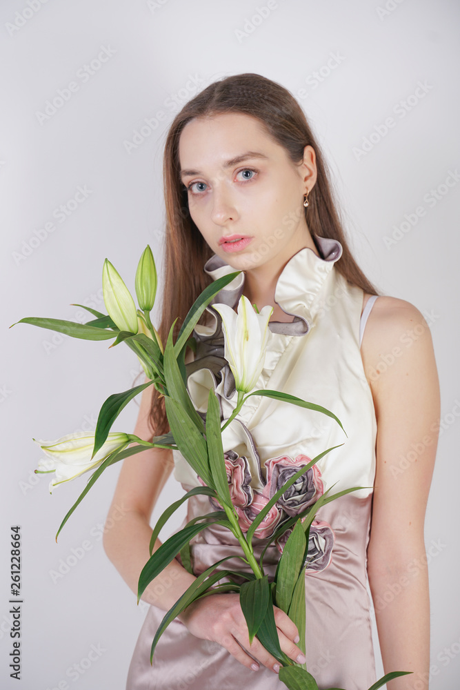 charming young caucasian girl in a pretty dress holds a lush Lily flower in her hands and stands on a white background in the Studio alone charming young caucasian girl in a pretty dress holds a lush Lily flower in her hands and stands on a white background in the Studio alone
