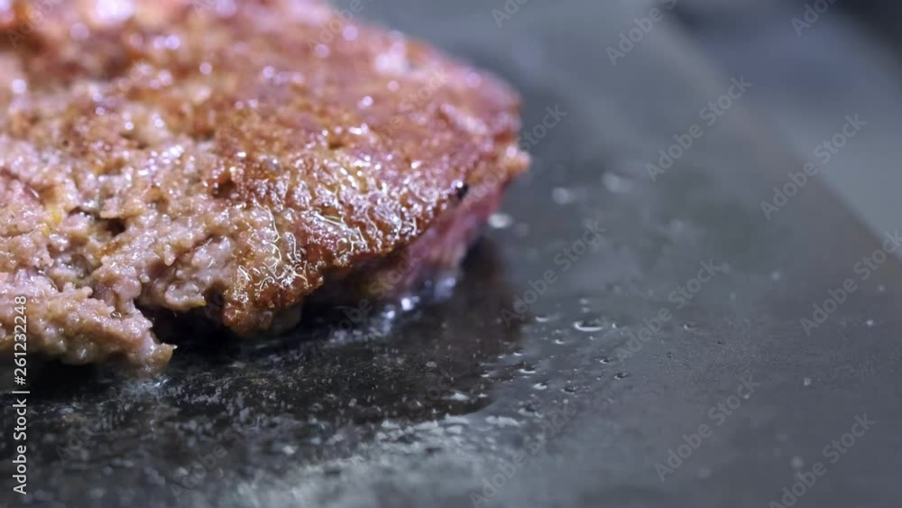 Cooking a hamburger, patty or steak. On a hot stove, a cook fries meat in a professional kitchen. The cook checks the readiness of the meat and turns the piece of meat over. Macro frame.