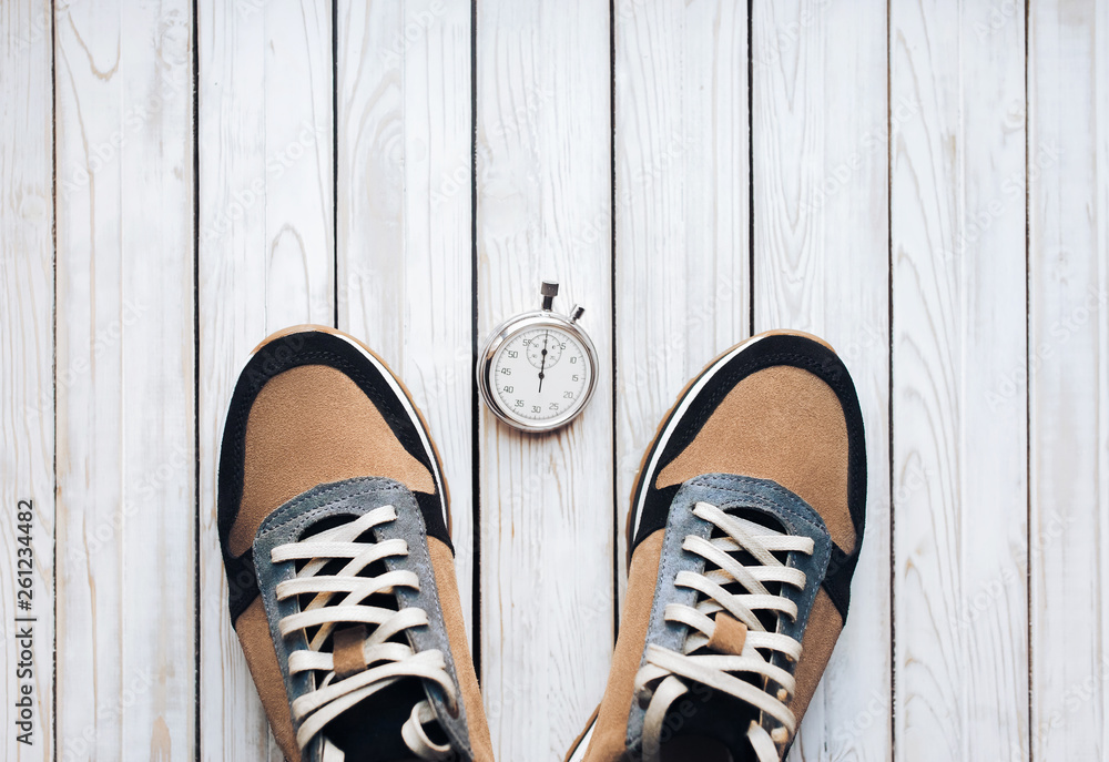 Two peige sport shoes (sneakers) from suede with stopwatch on white rustic wooden background. Training, jog and sport concept. Close up, top view.