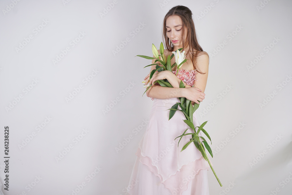 charming young caucasian girl in a pretty dress holds a lush Lily flower in her hands and stands on a white background in the Studio alone charming young caucasian girl in a pretty dress holds a lush Lily flower in her hands and stands on a white background in the Studio alone