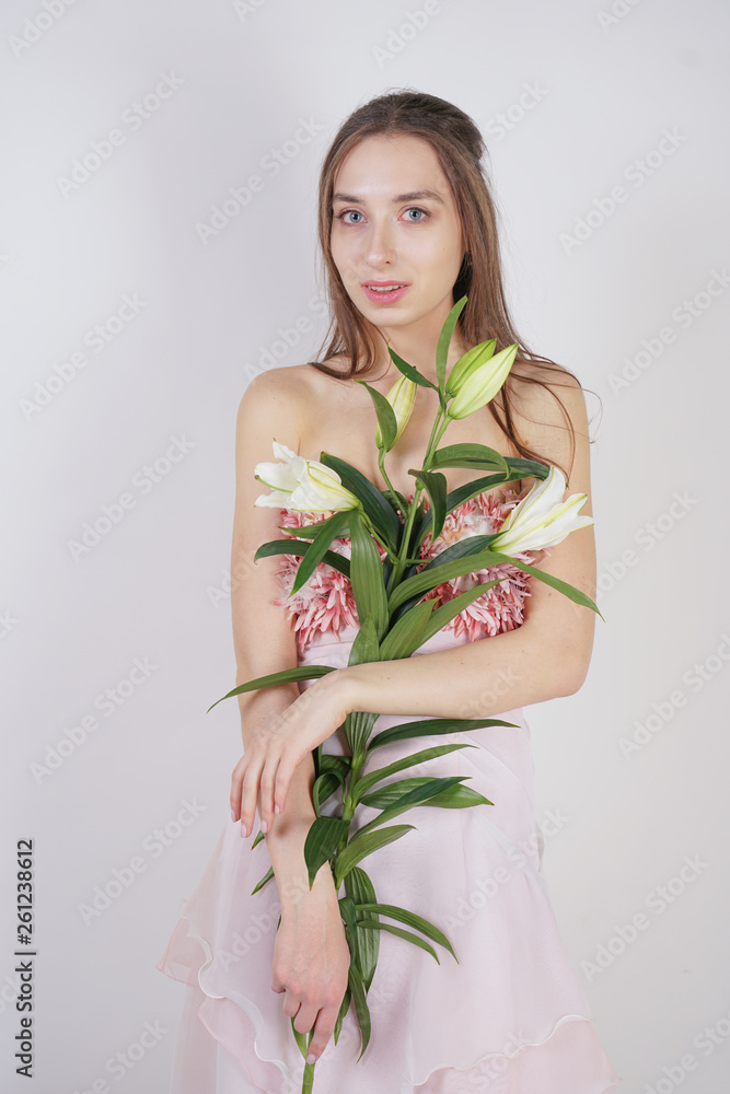 charming young caucasian girl in a pretty dress holds a lush Lily flower in her hands and stands on a white background in the Studio alone charming young caucasian girl in a pretty dress holds a lush Lily flower in her hands and stands on a white background in the Studio alone