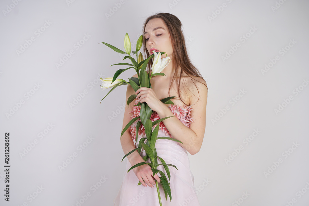 charming young caucasian girl in a pretty dress holds a lush Lily flower in her hands and stands on a white background in the Studio alone charming young caucasian girl in a pretty dress holds a lush Lily flower in her hands and stands on a white background in the Studio alone