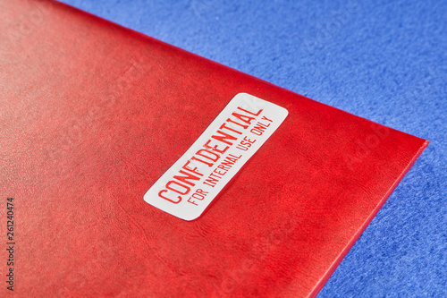 Red folder with the words Confidential for internal use only, on a blue velvet background. Close-up