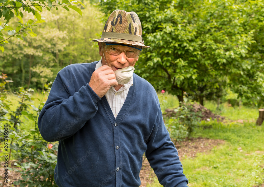Elderly man with safety glasses, mask and hat works in the garden.