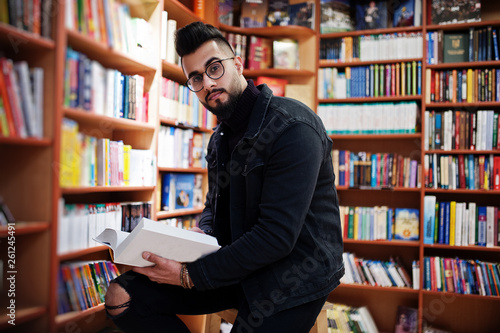 Tall smart arab student man, wear on black jeans jacket and eyeglasses, at library with book at hands.