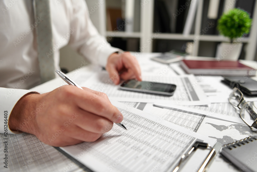 Fototapeta premium Businessman working at office and calculating finance, reads and writes reports. Business financial accounting concept.