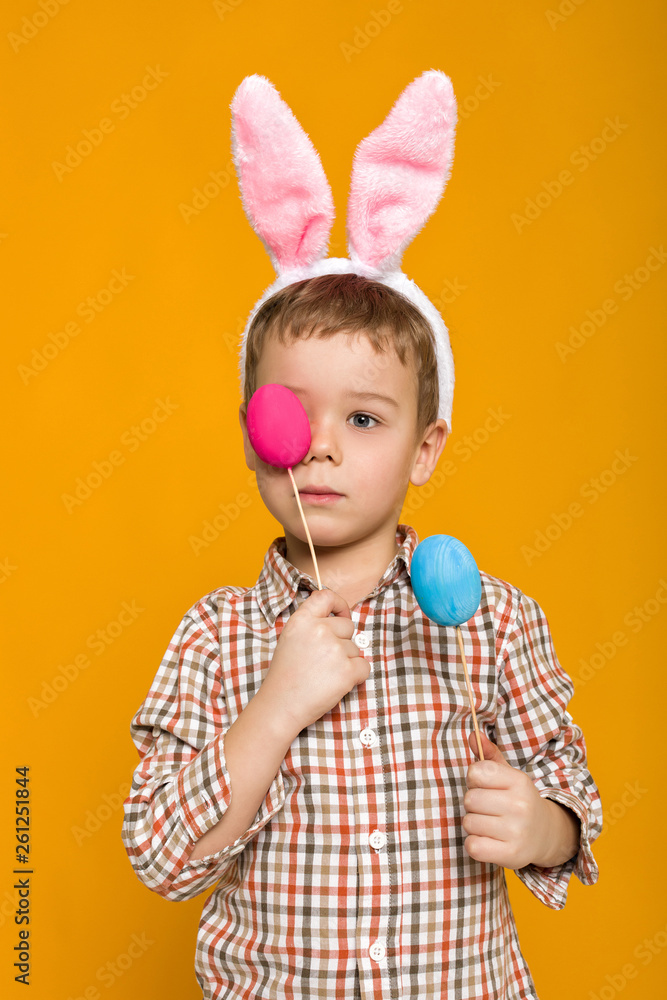 Portrait of cute little child boy with Easter bunny ears holding colorful eggs on yellow background. Happy easter