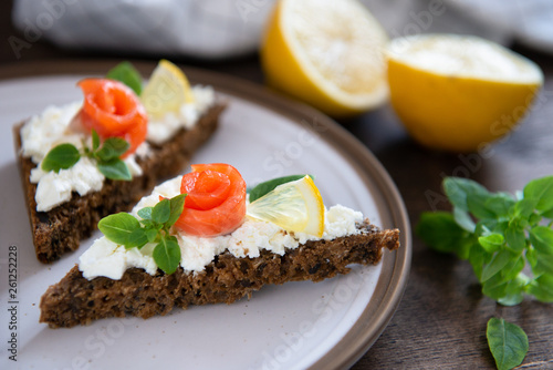 Sandwich with cereals bread, salmon, fresh cheese, basil and lemon on dark background. Close up