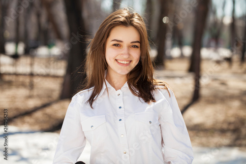 Young beautiful brunette girl in white shirt posing on spring park