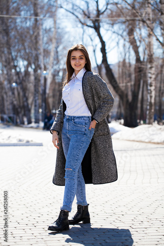 Brunette girl in a gray coat and blue jeans walks in spring park © Andrey_Arkusha