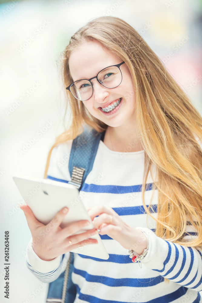 Portrait of a smiling beautiful teenage girl with dental braces. Young schoolgirl with school bag and tablet device Portrait of a smiling beautiful teenage girl with dental braces. Young schoolgirl with school bag and tablet device