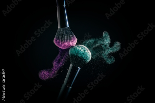 Cosmetic shades of different colors, red and blue, fly away from two make-up brushes creating a fancy pattern on a black background.