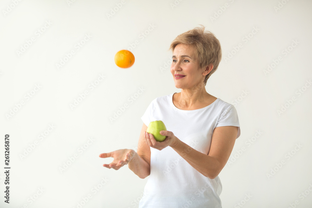 beautiful aged woman with short haircut in a white t-shirt with an apple and an orange on a white background beautiful aged woman with short haircut in a white t-shirt with an apple and an orange on a white background