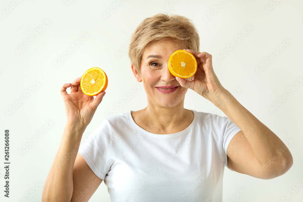 beautiful aged woman with a short haircut in a white T-shirt with oranges in her hands on a white background beautiful aged woman with a short haircut in a white T-shirt with oranges in her hands on a white background