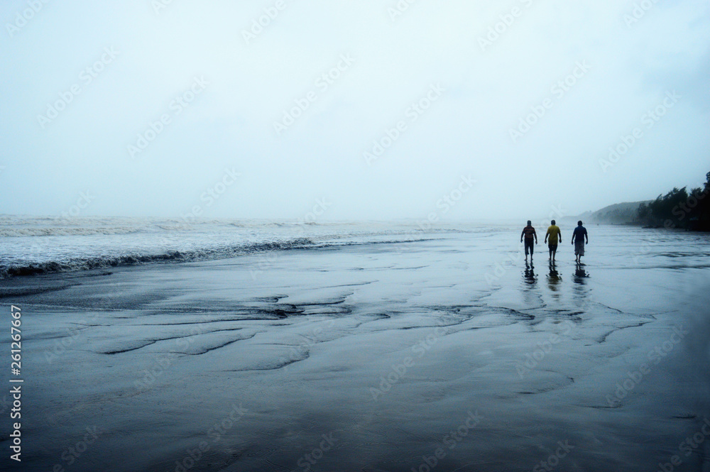 Three men walking in solitude on a beach.