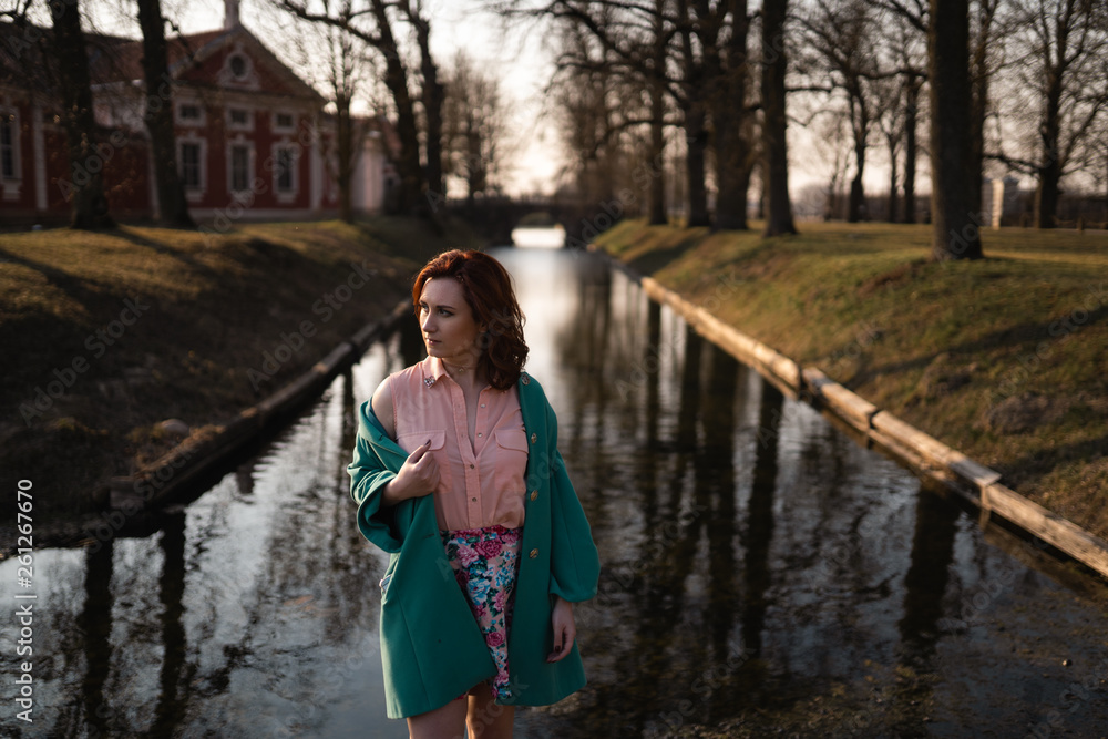 Beautiful young woman relaxing near a canal river in a park near the palace in Rundale, Latvia, 2019