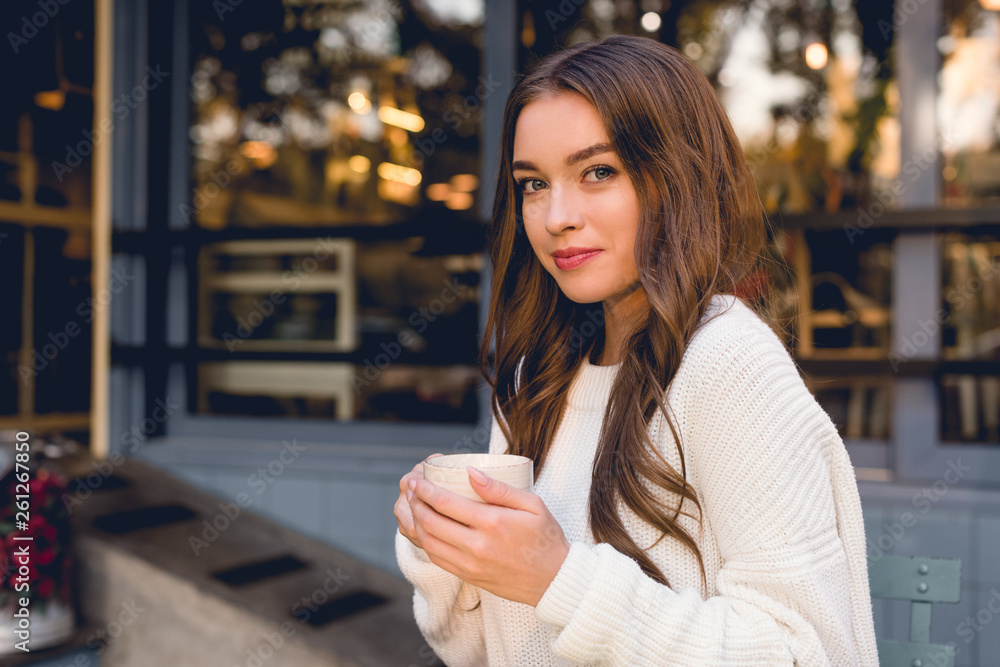 attractive young woman holding cup with coffee in cafe