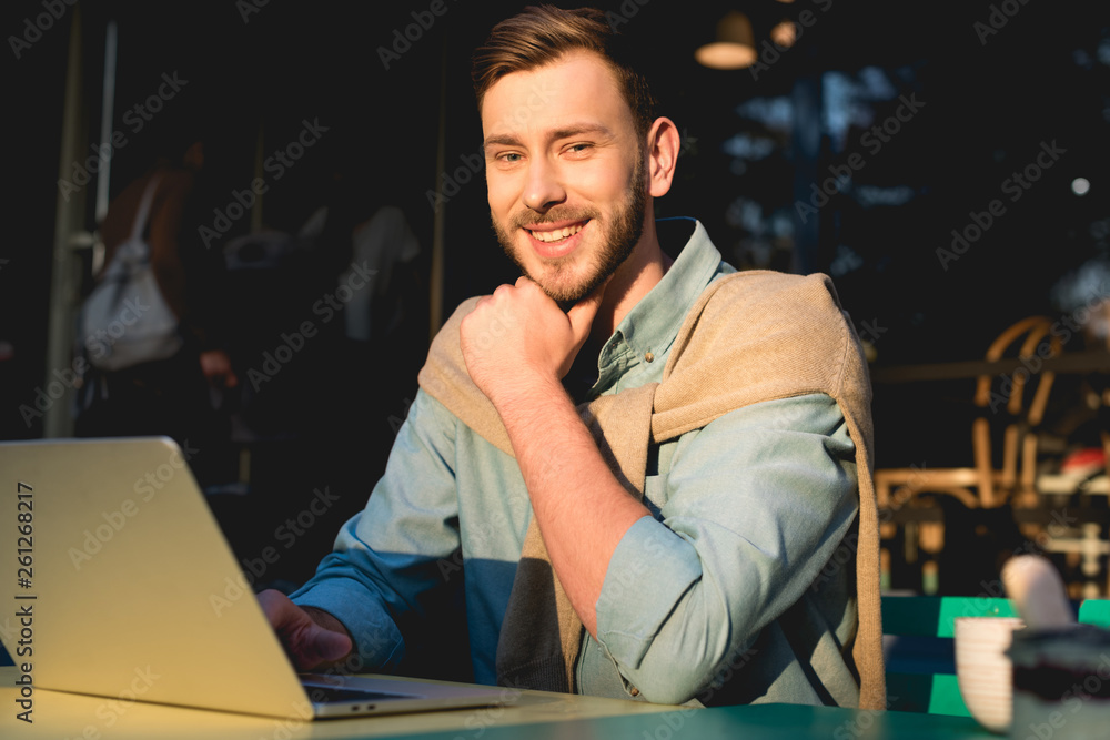 cheerful bearded freelancer sitting near laptop and looking at camera cheerful bearded freelancer sitting near laptop and looking at camera