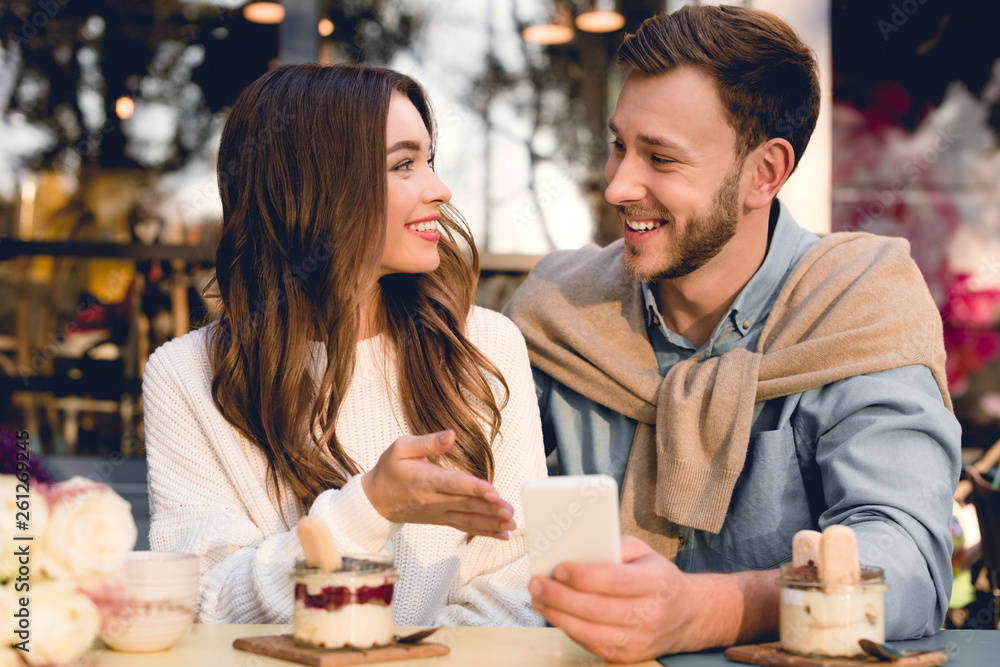 cheerful man looking at happy girl while holding smartphone