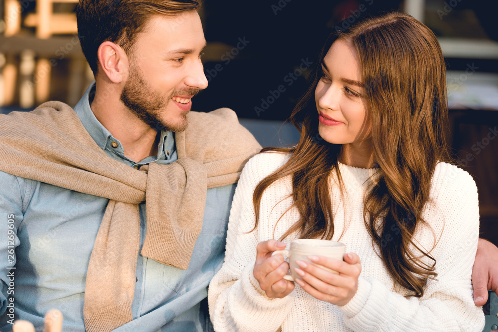 cheerful boyfriend looking at happy girlfriend holding cup of coffee cheerful boyfriend looking at happy girlfriend holding cup of coffee