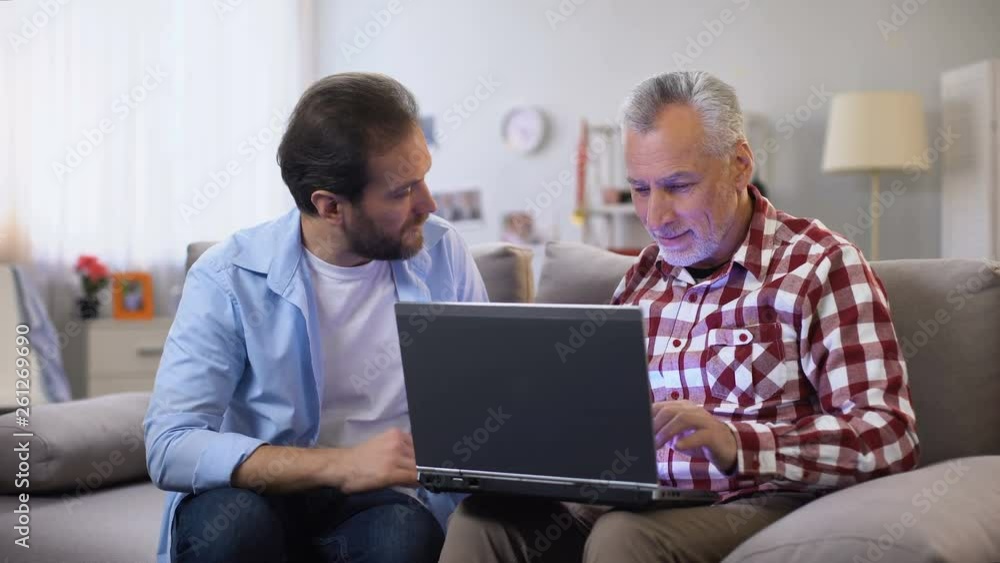 Young son explaining aged father how to use laptop, modern technologies, device Young son explaining aged father how to use laptop, modern technologies, device