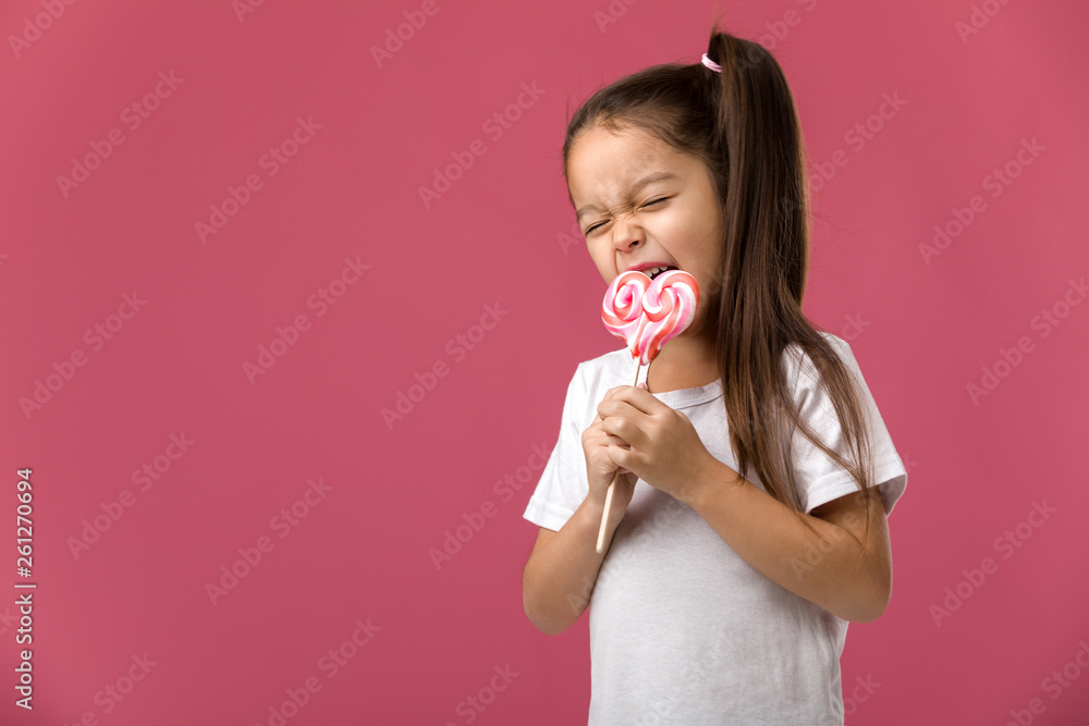 Beautiful cute little child girl eating sweet candy lollipop isolated on pink background Beautiful cute little child girl eating sweet candy lollipop isolated on pink background