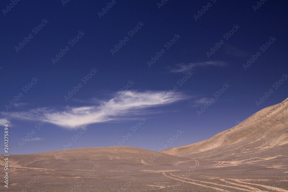 Naklejka premium Lost in the Landscapes of Atacama desert - Wheel tracks in barren arid sand plain in the nowhere contrasting with deep blue sky and few white cirrus clouds - Chile