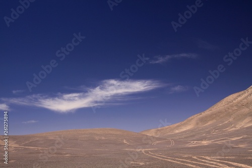 Lost in the Landscapes of Atacama desert - Wheel tracks in barren arid sand plain in the nowhere contrasting with deep blue sky and few white cirrus clouds - Chile