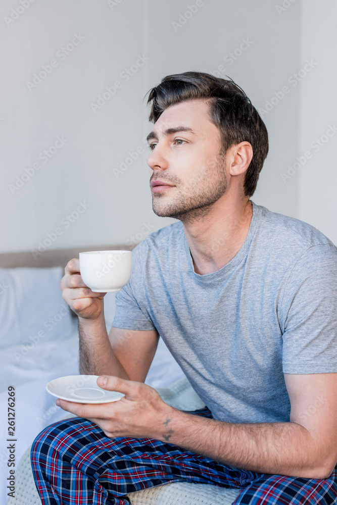 handsome pensive man sitting on bed and enjoying morning coffee handsome pensive man sitting on bed and enjoying morning coffee