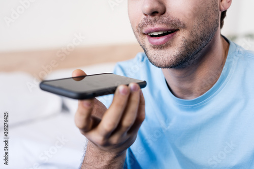 selective focus of smiling man talking on smartphone by speakerphone