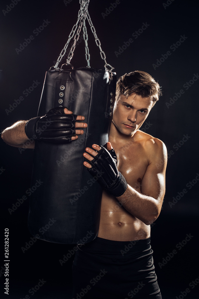 Serious boxer in gloves holding punching bag and looking at camera
