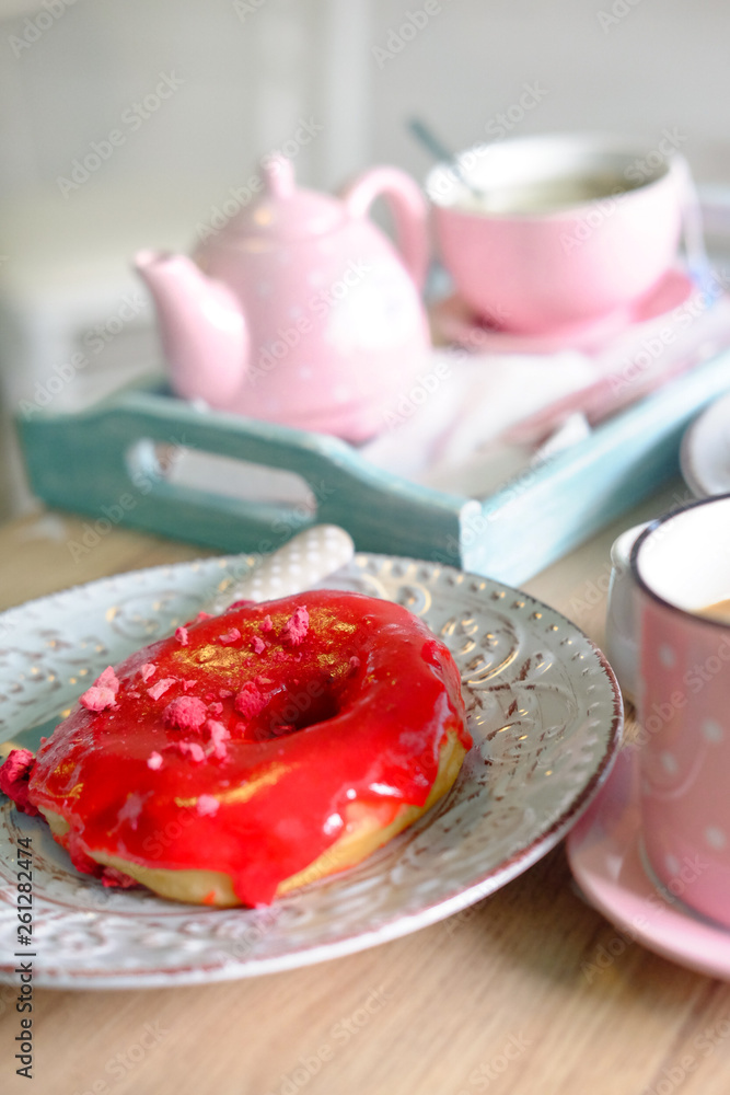 In the cafe. A pink cup of coffee with milk and amazing red donuts on table In the cafe. A pink cup of coffee with milk and amazing red donuts on table