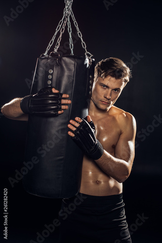 Serious boxer in gloves holding punching bag and looking at camera