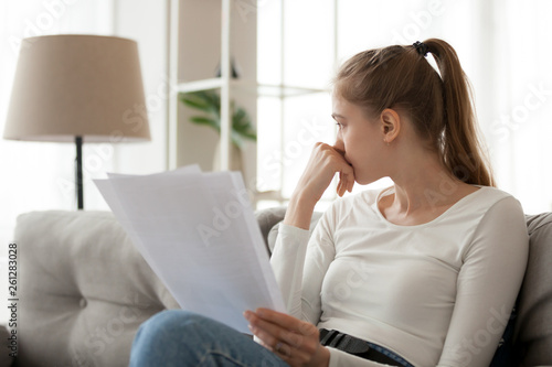Upset thoughtful woman holding paper document in hands, sitting on sofa photo