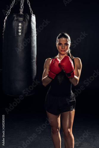Front view of boxer in red boxing gloves standing near punching bag on black © LIGHTFIELD STUDIOS