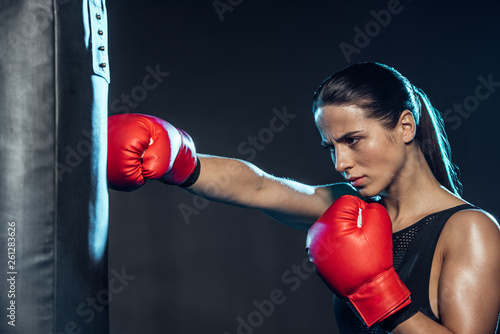 Tired boxer in red boxing gloves training with punching bag on black