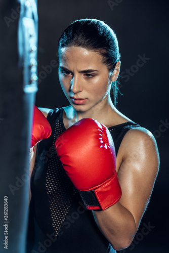 exhausted boxer in red gloves looking at punching bag on black