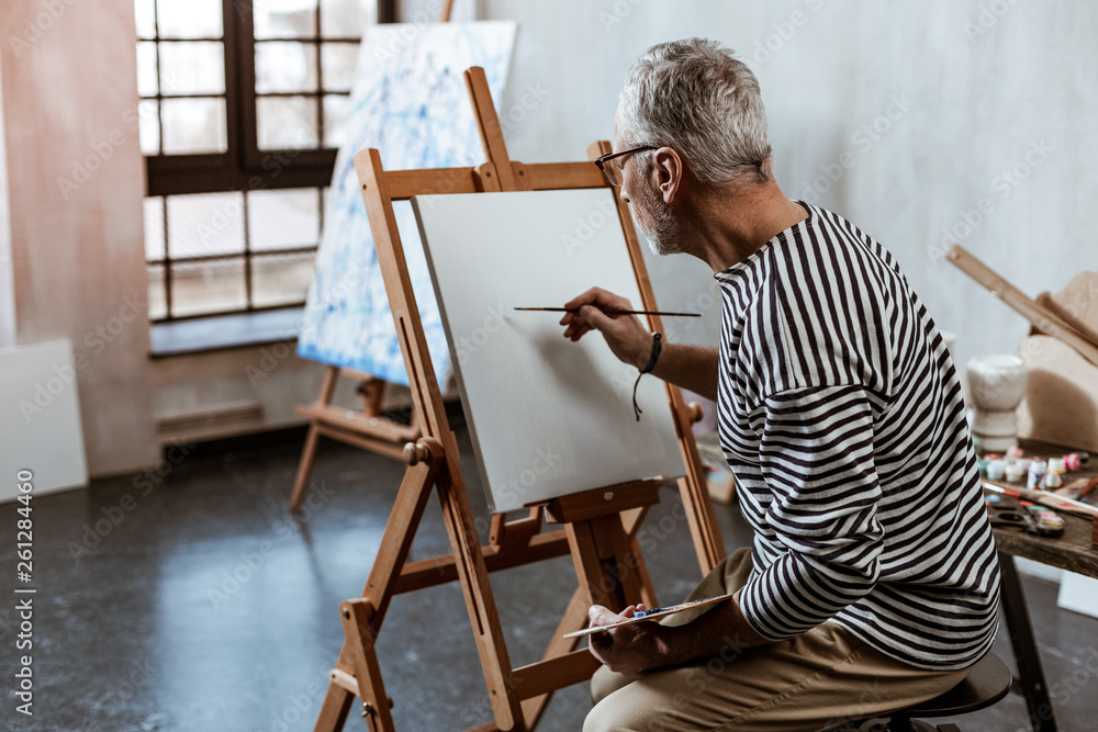 Artist sitting on chair near painting easel while working