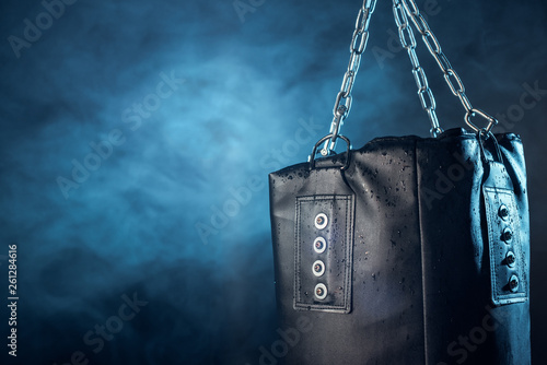 Leather punching bag hanging on steel chains on dark © LIGHTFIELD STUDIOS